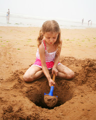 A Girl Digging at the Beach with a Blue Shovel