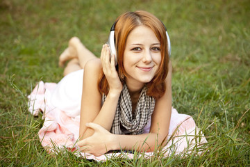 Young fashion girl with headphone lying at green grass