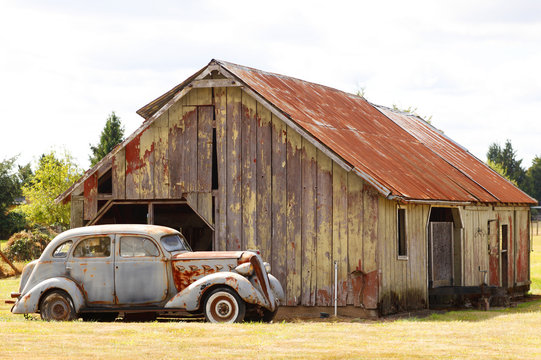 An old car next to a barn.