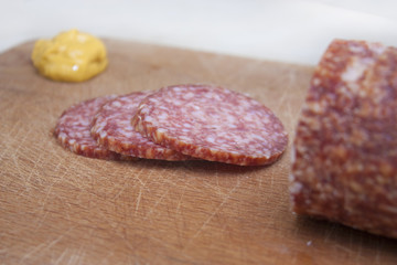 Sliced salami with mustard on wooden board