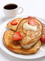 stack of pancakes with syrup, butter and strawberries