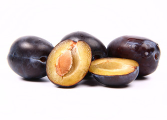 Plums on white background - one cut in half with a pit visible