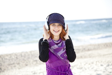 Portrait of red-haired girl with headphone on the beach.