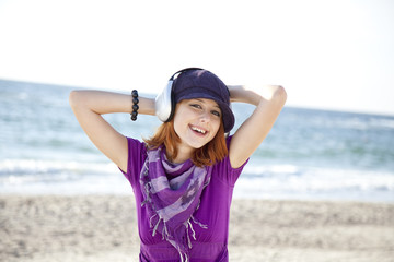 Portrait of red-haired girl with headphone on the beach.