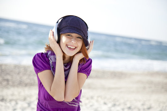 Portrait of red-haired girl with headphone on the beach.