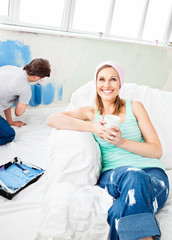 Smiling woman relaxing on a sofa while boyfriend painting the ro