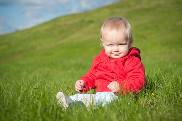 adorable smiling baby sitting on green grass within red jacket w