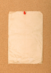 Wrinkled brown envelope attached to cork board with red pin.
