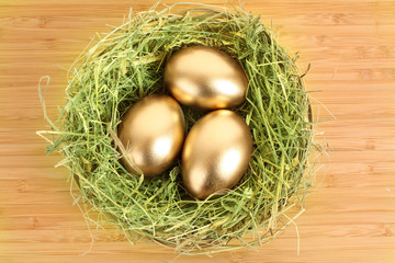 Three golden hen's eggs in the grassy nest on the wooden table