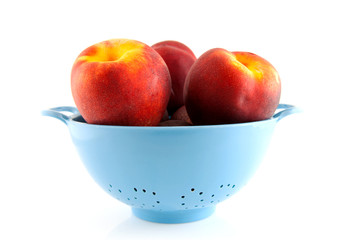 blue colander with peaches over white background