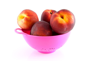 pink colander with peaches over white background