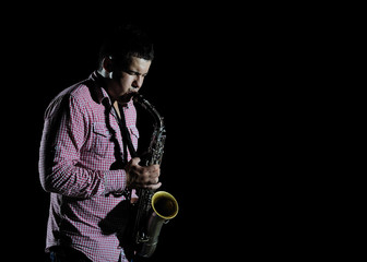 Fototapeta premium Young handsome man playing music on saxophone. black background