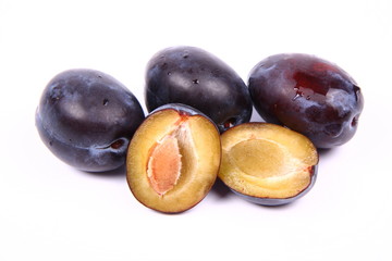 Plums on white background - one cut in half with a pit visible