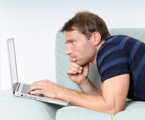 Young man relaxing with laptop on a couch and thinking