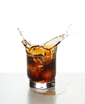 Glass with splashing whisky drink on a white background