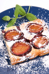 Piece of Plum Pie covered with powder sugar on a blue plate