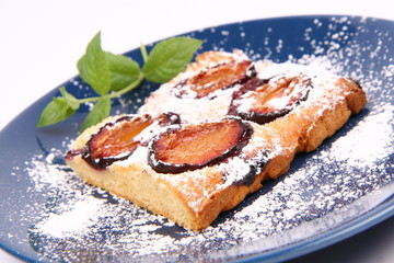 Plum Pie covered with powder sugar on a plate with a mint twig