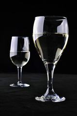 Two wine glasses with white wine on a black background.