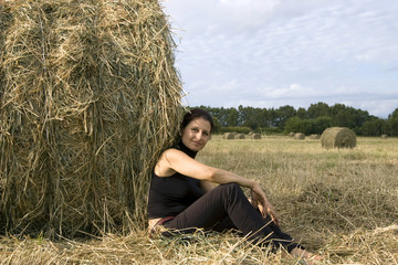 Naklejka na ściany i meble woman sits in the field about a haystack
