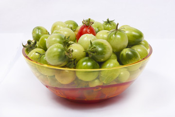 Green tomatoes and a red one in bowl