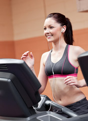 Fototapeta na wymiar Smiling athletic woman training on a running machine with earpho