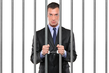 A handcuffed businessman in jail holding bars