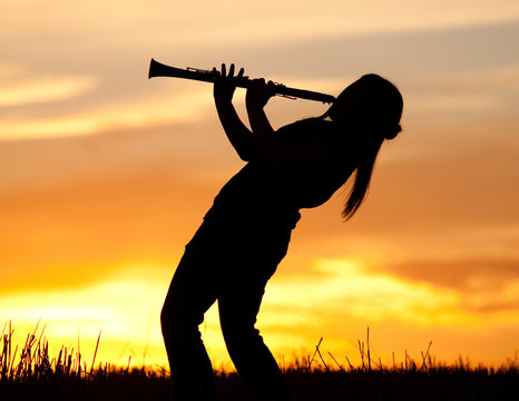 A silhouetted woman plays the Clarinet at sunset.