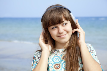 Young brunet girl with headphone on the beach.