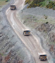 Three Large Lorry Trucks Driving Down a Quarry Incline.