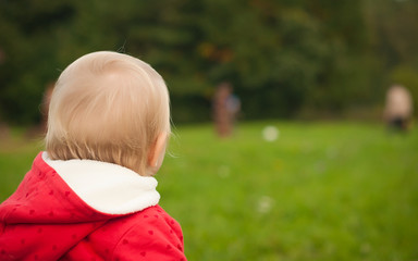 young adorable baby stay on grass in park watching ball game