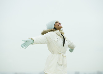 Mixed race woman standing in snow with arms outstretched