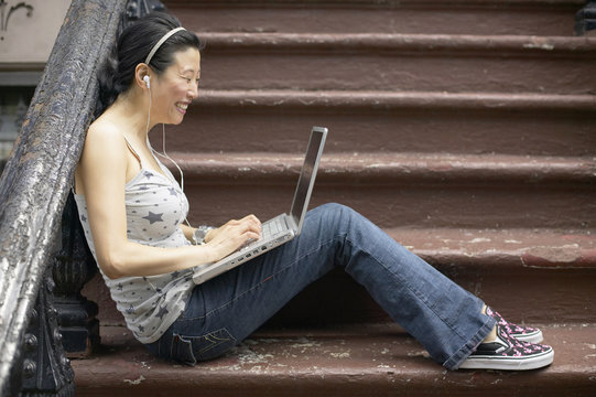 Asian woman sitting on front steps with laptop