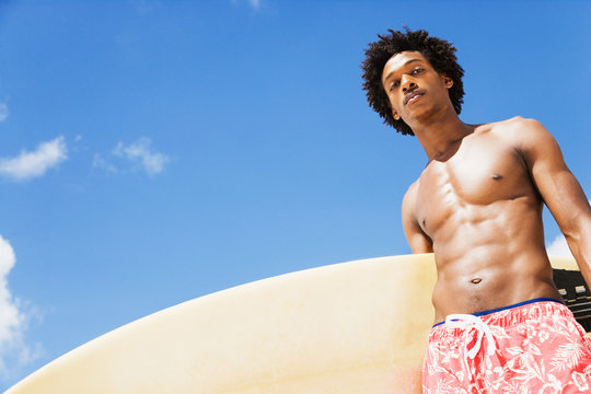 Serious African man holding surfboard