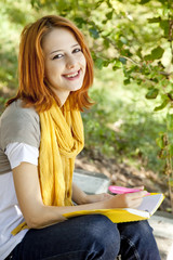 Obraz premium Red-haired student girl with notebook sitting at outdoor.