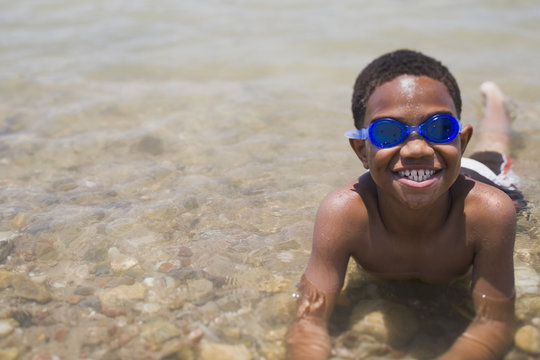 African boy wearing goggles and laying in shallow lake