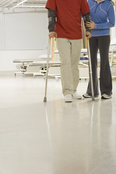 Woman helping man walk on crutches in hospital