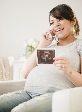 Pregnant Hispanic woman with sonogram picture talking on phone