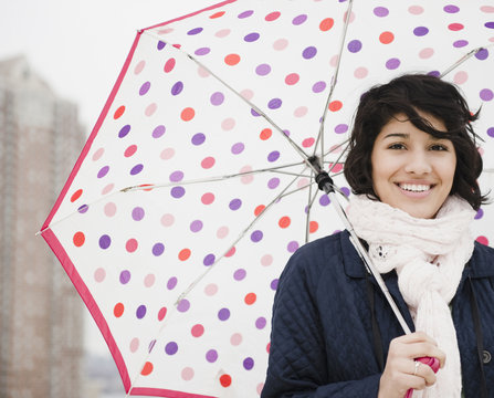 Hispanic woman walking in city with umbrella