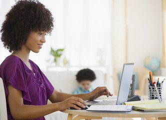 Mother working on laptop with child in background
