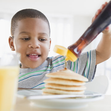 African American boy pouring syrup on pancakes