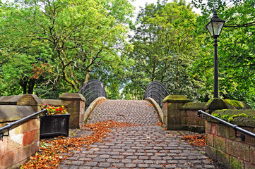 Crossing the old bridge amongst the trees via a traditional cobbled footpath  in the pretty village of Worsley near Manchester