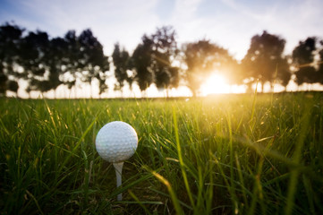 Golf ball on tee on gold course at sunset