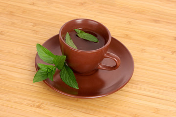 Cup of green tea on the saucer with mint on wooden surface