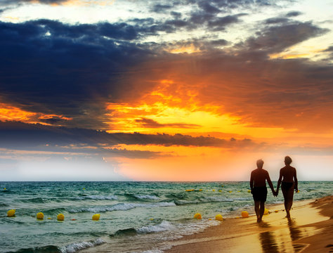 Lovers walk along the beach at sunset.