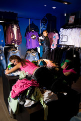Fototapeta na wymiar Pair of young adults in dress store. Girl lays on pile of shirts