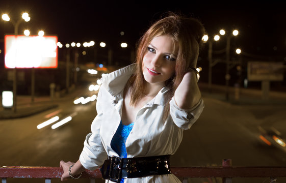 Beautiful young woman standing on illuminated street at night