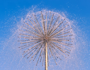 Fountain as dandelion on a blue sky background