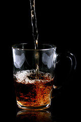 pouring tea to a transparent teacup on black background