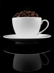 Cup of coffre with coffee beans on reflected black background