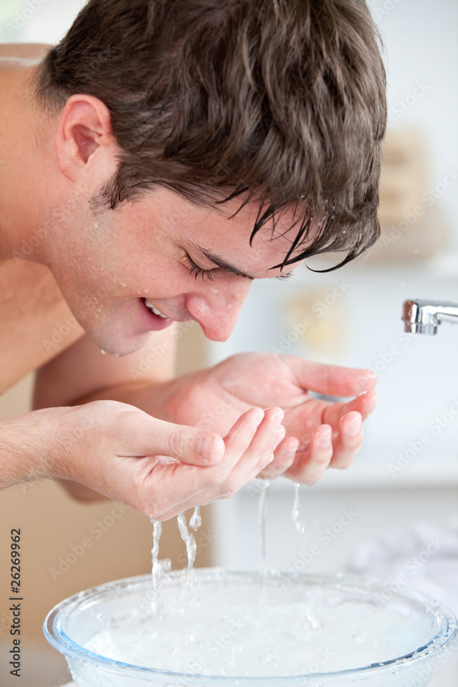 Wall mural Smiling caucasian man spraying water on his face after shaving i